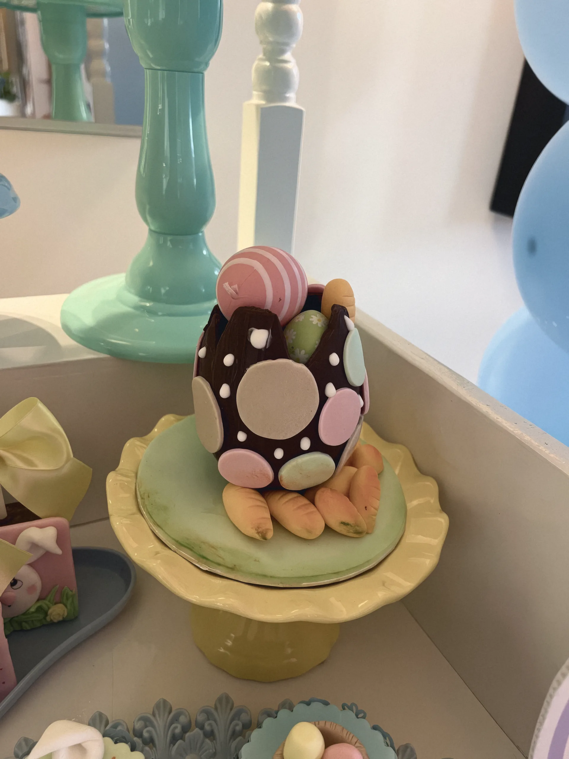 A hand-decorated chocolate Easter egg on a pastel cake stand